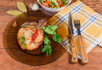 Grilled pork loin chop bone-in on dish, fork, knife