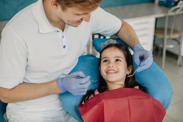 Beautiful Little girl sitting in stomatology chair looking at her dentist smiling before doing a teeth surgery