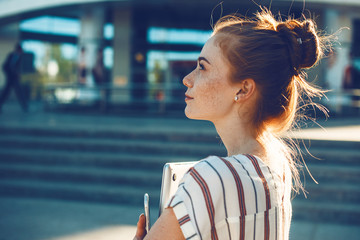 Side view portrait of a beautiful young female entrepreneur looking away holding a laptop against a...