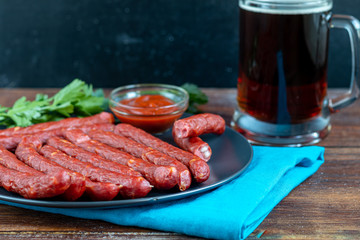 Smoked sausages on a dark plate. Nearby a large glass of dark beer. Copy space.