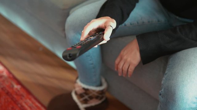 Female hand holding the TV remote control and turn 0n or off smart tv. Channel surfing, focused on the hand and remote control.