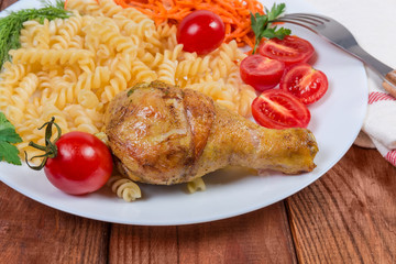 Fried chicken leg against cooked spiral pasta, vegetables, close-up