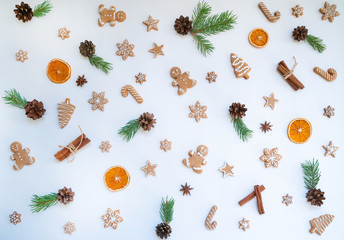 Pattern made with spruce branches and Сhristmas decoration on pastel background. Christmas objects view from above. Christmas gingerbread, cinamon, dry orange and decorative ornaments.