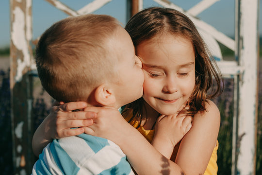 Close up portrait of a lovely little kid embracing and kissing his sister outdoor at the sunset.