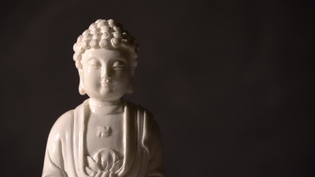 White Buddha figurine rotates on a black grange background