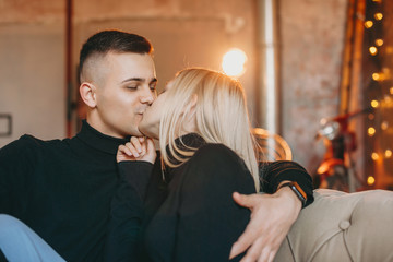 Charming young couple embracing on the couch kissing in their room at hotel while traveling.