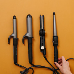 Set of curling irons with hair straightener over orange. Top view