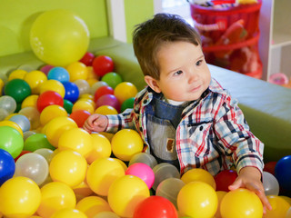 Fototapeta na wymiar child plays in colored balls. plastic balls in the playroom. Happy little kid boy playing at colorful plastic balls playground high view. Adorable child having fun indoors