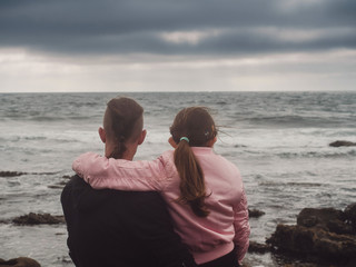 Brother and sister watching oceans wave. Dramatic sky, Concept family, relationship, outdoors activity.