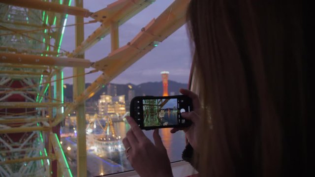 Woman using iphone to take pictures while riding a large ferris wheel at Kobe port Japan