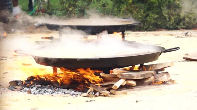Firewood cooking paellas outdoor with steaming smoke, medium shot 