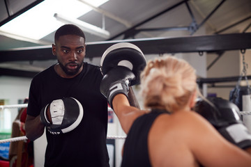 Male Personal Trainer Sparring With Female Boxer In Gym Using Training Gloves