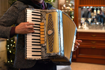 A man playing accordion indoors on retro party with decorated Christmas tree on the back