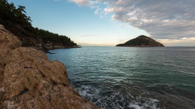 Time lapse with sunset at the rocky coastline of Thasos island and view to little island Nisida Kinira, Greece