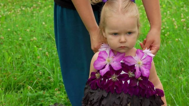Woman put on girl a beautiful purple fantasy dress made of flowers and leaves