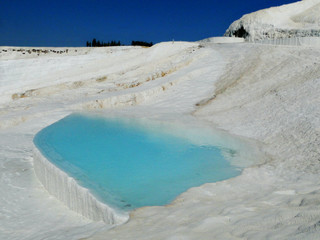 Natural spring water in white travertine terrace formations, covered by carbonate mineral, turns into powder blue color under sunlight. Travel destination in Pamukkale, Cotton Castle in Turkey. 