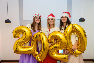 Three cheerful happy girls in santa hats posing with gold number balloons 2020 on party celebration