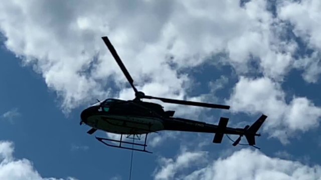 Helicopter Flying Against Blue Sky and Clouds with a Steel Cable in Switzerland.