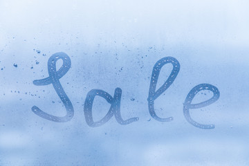 The creative inscription sale on the blue evening or morning window glass with drops 