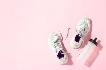 White sneakers and a bottle of water under morning sunlight on a pink background. Concept, jogging, running, fitness, cross fit. Morning run. Banner. Flat lay, top view - obrazy, fototapety, plakaty