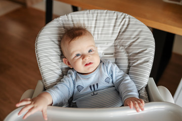 Nervous hungry baby boy sitting in his chair and waiting for his mother to bring him baby food while sitting in his chair.