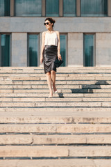 Fashionable brunette businesswoman in leather pencil skirt and sunglasses walking on stairs