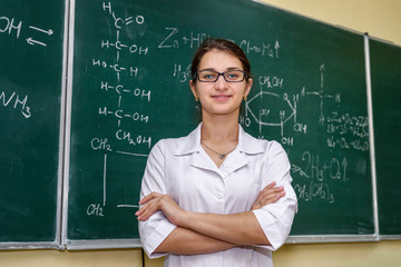 Female portrait. Chemistry teacher standing near class board pointing on it