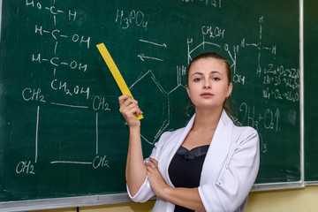 Female portrait. Chemistry teacher standing near class board pointing on it