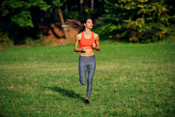 Full length of attractive fit caucasian brunette in sportswear and with ponytail running on meadow. Sunny morning in nature.