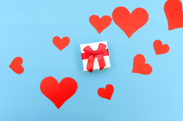 Gift box among red paper hearts on a blue background. Top view, copy space. Valentine's day, a symbol of love. Festive background