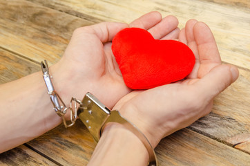 Man's handcuffed hands hold red heart on wooden background, copy space