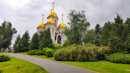 Beautiful christian church with golden domes among green trees. Church building on a sunny summer day.