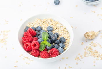 Breakfast smoothie bowl with granola, fresh raspberries, blueberries and mint on white background. Healthy food.