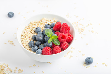 Breakfast smoothie bowl with granola, fresh raspberries, blueberries and mint on white background. Healthy food.
