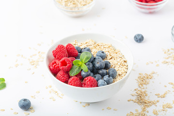 Breakfast smoothie bowl with granola, fresh raspberries, blueberries and mint on white background. Healthy food.