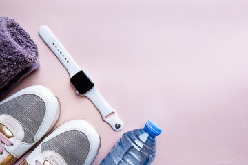 Top view of sport accessories for fitness and running. Training shoes, towel, fitness bracelet watch and water isolated on pink background.