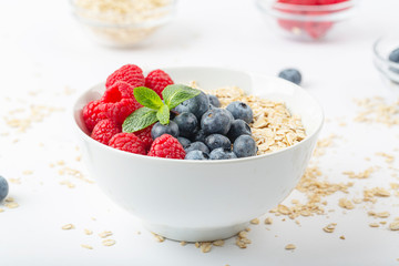 Breakfast smoothie bowl with granola, fresh raspberries, blueberries and mint on white background. Healthy food.
