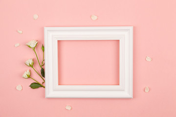 Minimal composition with a white photo frame and rose flowers on a pink pastel background. Layout with copy space