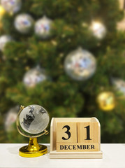 Naklejka premium Day 31 of december month, wooden calendar and gobal glass earth map with christmas tree background.