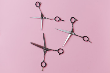 Three pairs of metal hairdresser scissors in an equally open position over pink