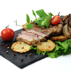 sliced ​​piece of baked meat closeup, served on a dark stone board with fresh and fried vegetables on a white background isolated