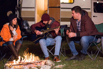 Friends relaxing and playing on guitar around camp fire