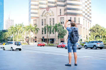 Obraz premium Man tourist travel and photo for social media in Kuala Lumpur, Malaysia. Man tourist taking photo of the city by mobile phone.