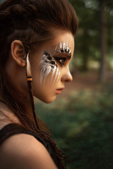 Attractive female hunter with tribal makeup posing in forest 