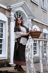 Young woman in a vintage dress stands with a basket of apples at the railing of an ancient staircase