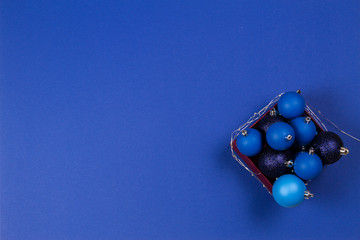 Blue Christmas bauble balls and garland in the box on blue background. Top view