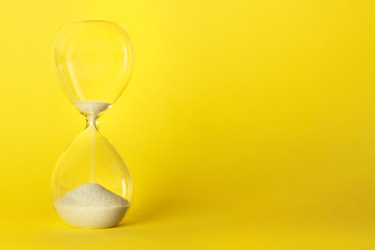 Time is running out concept. An hourglass on a vibrant yellow background with a place for text
