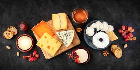 Cheese board panorama with wine and fruit, a flat lay, shot from the top on a black background