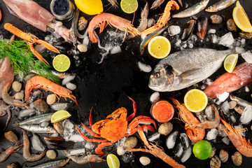 Fish and seafood variety, a flat lay overhead shot, a frame with copy space on a black background. Sea bream. shrimps, crab, sardines, squid, mussels and other fresh products with a place for text