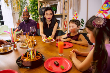 Portrait of happy multiethnic family celebrating a birthday at home. Big family eating snacks and drinking wine while greeting and having fun children. Celebration, family, party, home concept.